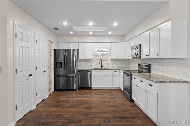 kitchen with appliances with stainless steel finishes, sink, white cabinets, light stone counters, and dark wood-type flooring