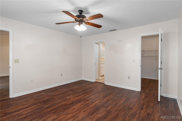 unfurnished bedroom featuring dark wood-type flooring, ensuite bath, a spacious closet, a closet, and ceiling fan