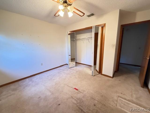 unfurnished bedroom featuring a closet, a textured ceiling, light colored carpet, and ceiling fan