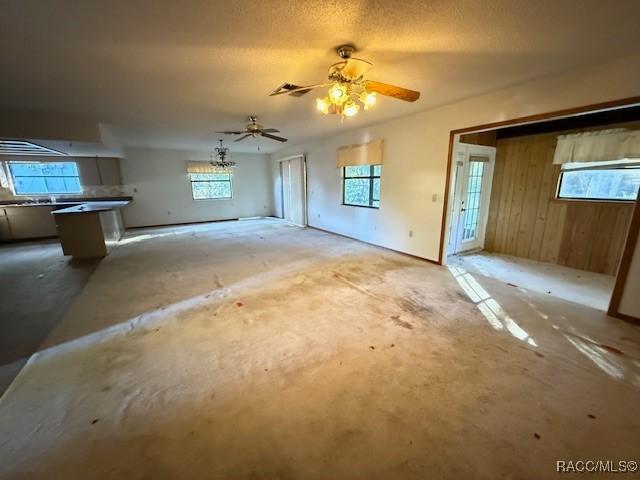 unfurnished living room featuring ceiling fan, wood walls, and a textured ceiling