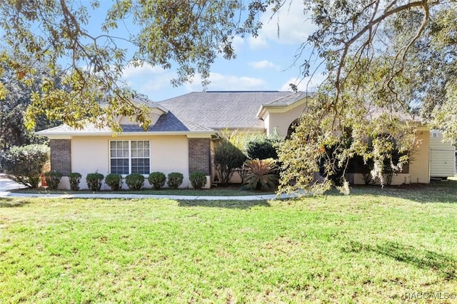 view of front of home with brick siding, stucco siding, a front yard, and a shingled roof