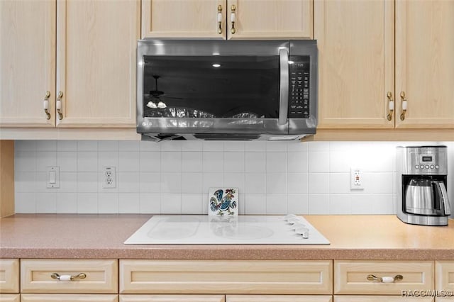 kitchen featuring light countertops, stainless steel microwave, backsplash, light brown cabinets, and white electric cooktop