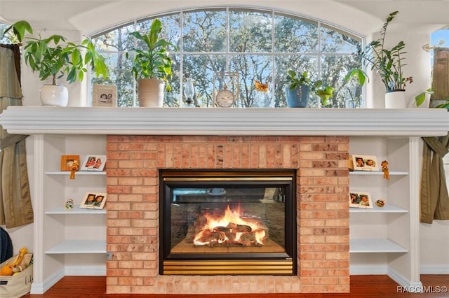 interior details featuring built in shelves, a fireplace, wood finished floors, and baseboards