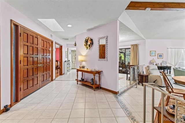 entrance foyer featuring vaulted ceiling with skylight, light tile patterned floors, and a textured ceiling