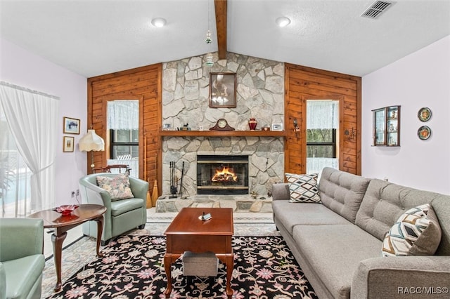 living room with a stone fireplace, wood walls, a textured ceiling, and vaulted ceiling with beams