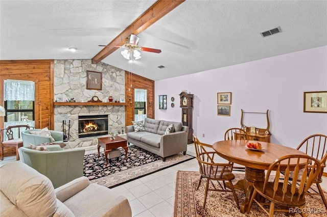 living room with a textured ceiling, ceiling fan, a fireplace, vaulted ceiling with beams, and light tile patterned flooring