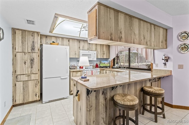 kitchen with kitchen peninsula, white appliances, light stone countertops, and a breakfast bar