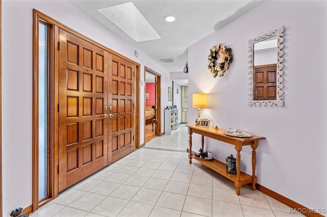 foyer entrance featuring light tile patterned floors, a textured ceiling, and a skylight