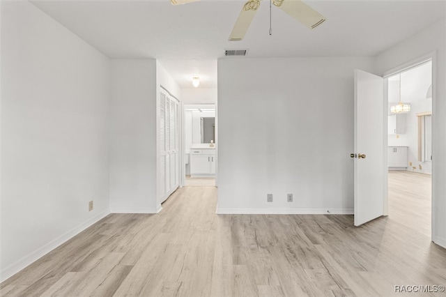 spare room with ceiling fan with notable chandelier and light hardwood / wood-style flooring