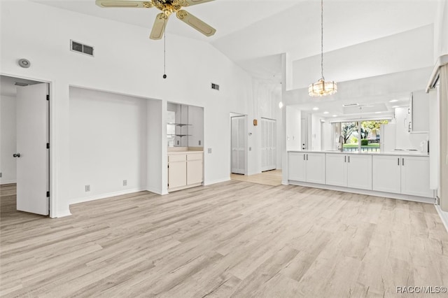 unfurnished living room featuring high vaulted ceiling, ceiling fan with notable chandelier, and light wood-type flooring