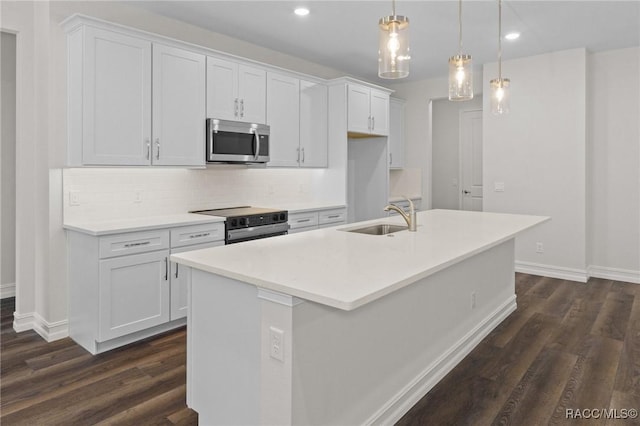 kitchen featuring stainless steel microwave, electric stove, a sink, an island with sink, and dark wood finished floors