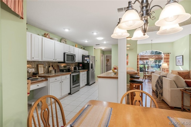 kitchen with pendant lighting, appliances with stainless steel finishes, white cabinetry, light tile patterned flooring, and decorative backsplash