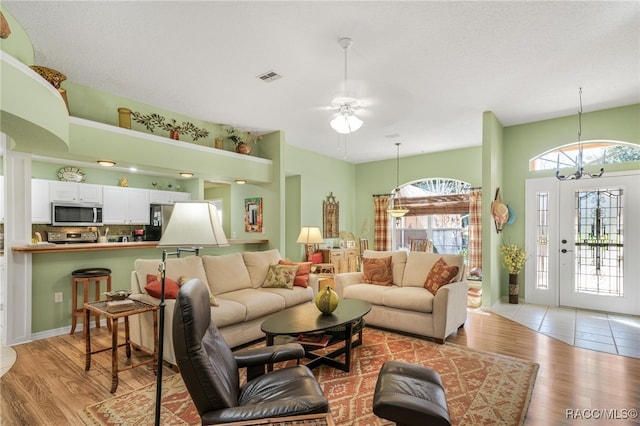 living room with ceiling fan with notable chandelier and light hardwood / wood-style floors