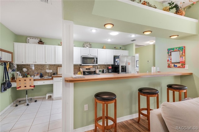 kitchen with stainless steel appliances, white cabinetry, a breakfast bar, and kitchen peninsula