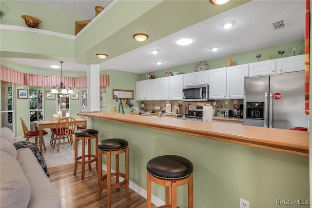 kitchen with a kitchen bar, white cabinetry, kitchen peninsula, pendant lighting, and stainless steel appliances