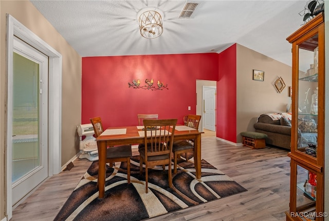 dining area featuring a textured ceiling, vaulted ceiling, and light hardwood / wood-style flooring