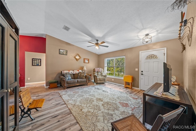 living room featuring a textured ceiling, light wood-type flooring, ceiling fan, and lofted ceiling