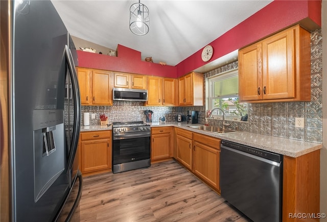 kitchen featuring appliances with stainless steel finishes, tasteful backsplash, vaulted ceiling, sink, and light hardwood / wood-style flooring