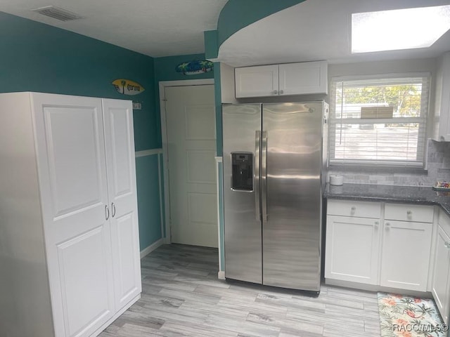 kitchen with visible vents, decorative backsplash, white cabinets, light wood-style floors, and stainless steel fridge