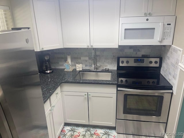 kitchen featuring dark stone counters, decorative backsplash, stainless steel appliances, white cabinetry, and a sink