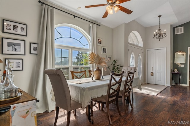 dining area with ceiling fan with notable chandelier, a towering ceiling, and dark hardwood / wood-style flooring