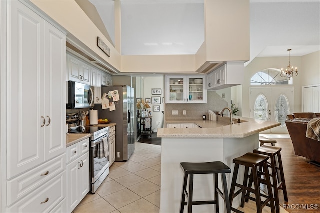 kitchen with kitchen peninsula, white cabinetry, stainless steel appliances, and light hardwood / wood-style flooring