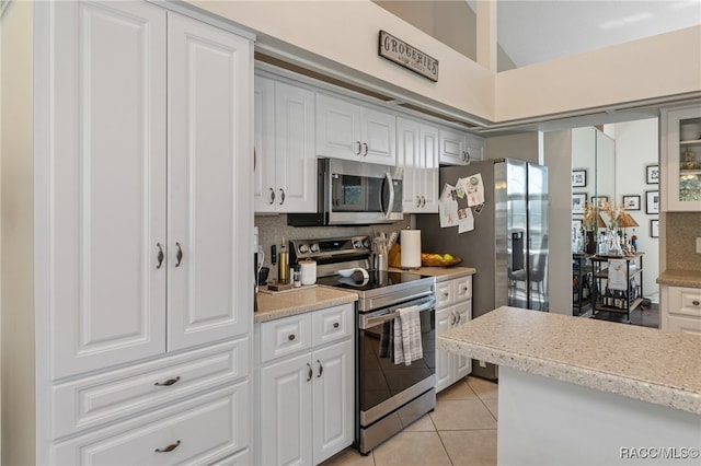 kitchen with white cabinets, light tile patterned floors, stainless steel appliances, and tasteful backsplash