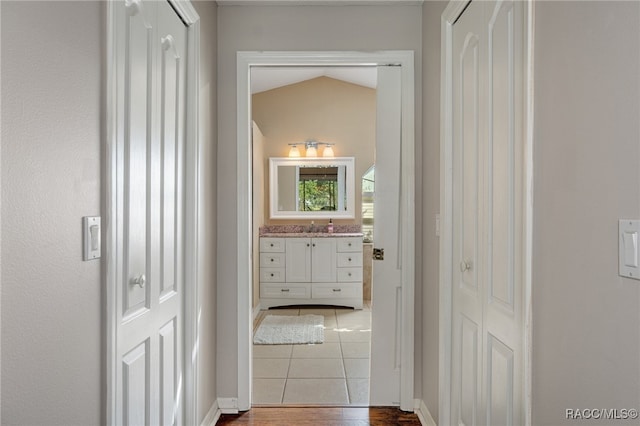 corridor with hardwood / wood-style floors, lofted ceiling, and sink