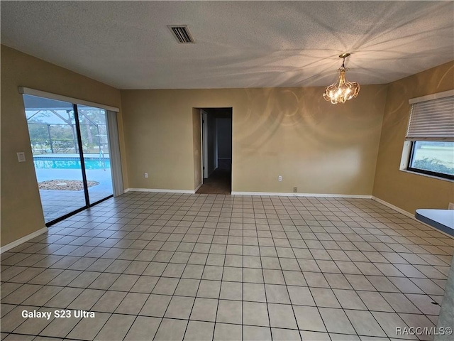 tiled empty room featuring a wealth of natural light, a chandelier, and a textured ceiling