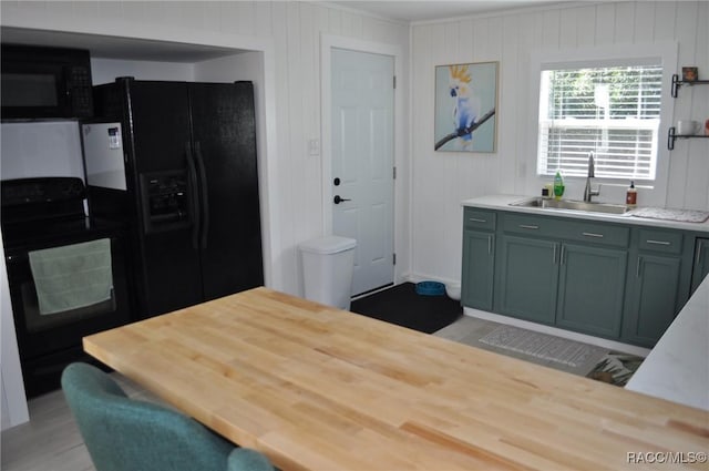 kitchen featuring sink, green cabinets, wooden walls, black appliances, and light hardwood / wood-style floors