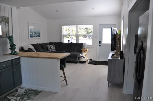 living room with lofted ceiling, light wood-type flooring, and wood walls