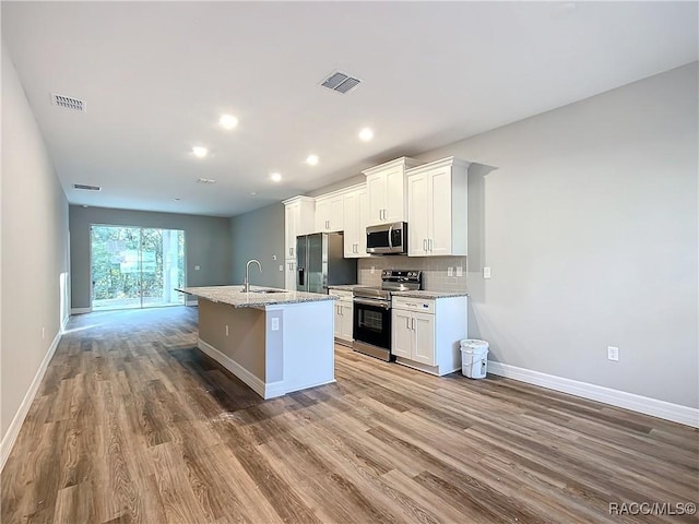 kitchen with white cabinetry, wood-type flooring, a kitchen island with sink, stainless steel appliances, and light stone countertops