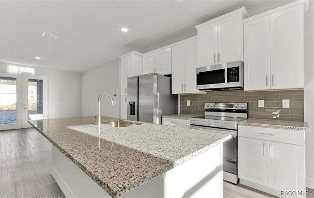 kitchen with white cabinets, stainless steel appliances, a center island with sink, and light hardwood / wood-style floors