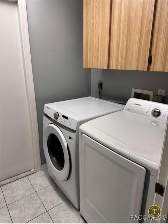 laundry area featuring washer and clothes dryer, light tile patterned floors, and cabinet space