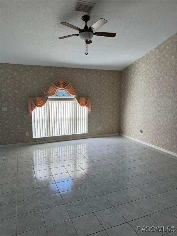 tiled empty room featuring visible vents, baseboards, ceiling fan, and wallpapered walls