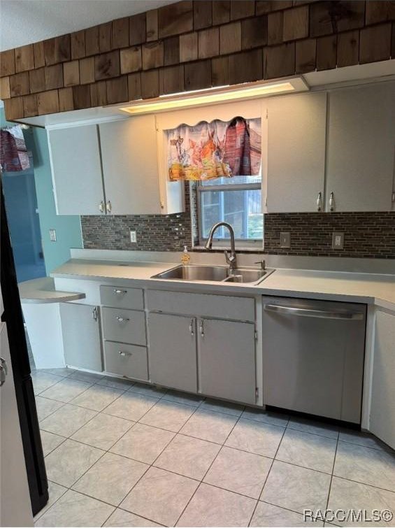 kitchen with stainless steel dishwasher, light countertops, backsplash, and a sink