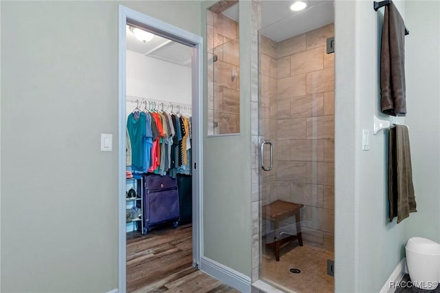 bathroom featuring a spacious closet, a stall shower, wood finished floors, and baseboards