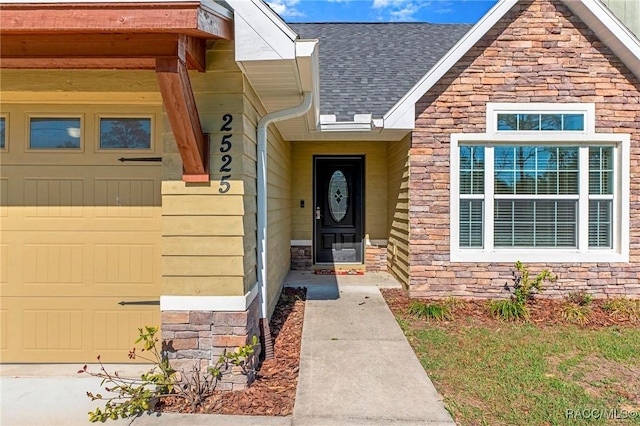 view of exterior entry featuring a garage, stone siding, and roof with shingles