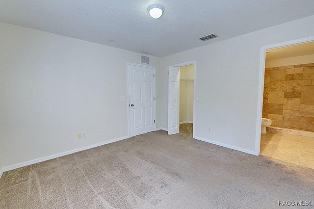 unfurnished bedroom featuring ensuite bathroom, a textured ceiling, a spacious closet, light colored carpet, and a closet