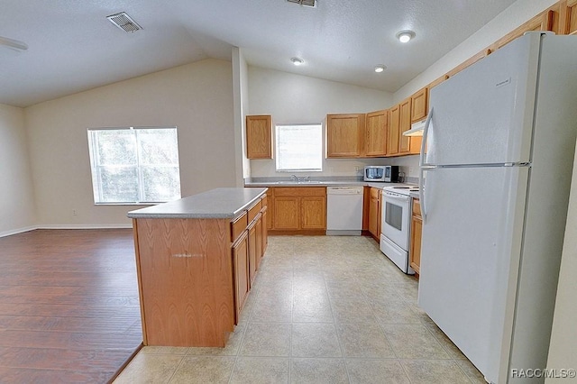 kitchen featuring vaulted ceiling, white appliances, a center island, and sink