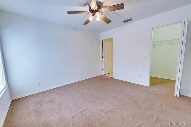 unfurnished bedroom with a walk in closet, light colored carpet, a textured ceiling, a closet, and ceiling fan