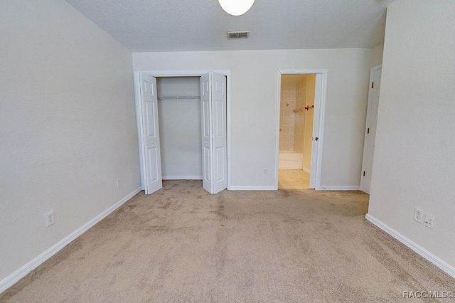 unfurnished bedroom with light carpet, a closet, a textured ceiling, and ensuite bathroom