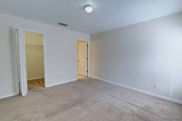 unfurnished bedroom featuring light carpet, a walk in closet, a closet, and a textured ceiling