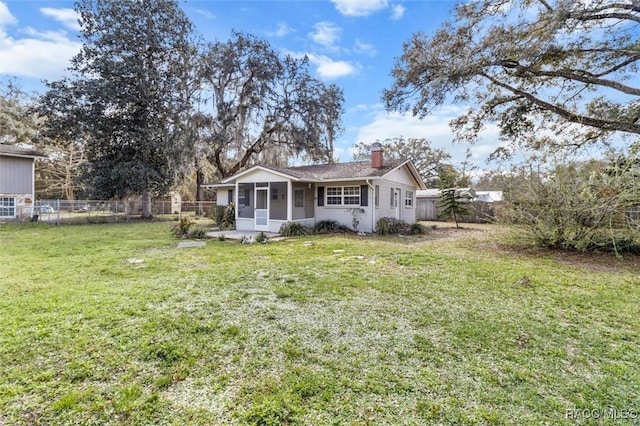 view of front of property featuring a front lawn, a chimney, a fenced backyard, and a sunroom