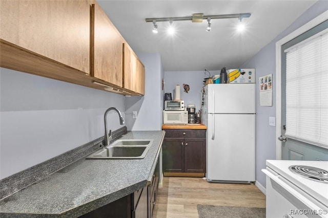 kitchen featuring dark countertops, white appliances, light wood-type flooring, and a sink