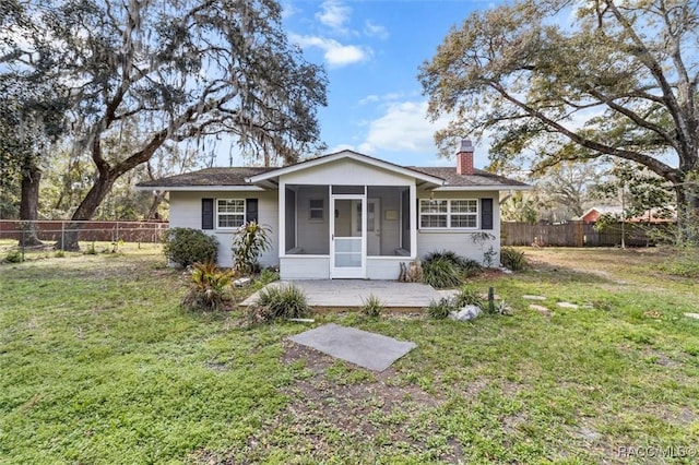 view of front facade featuring a sunroom, a chimney, fence, and a front lawn