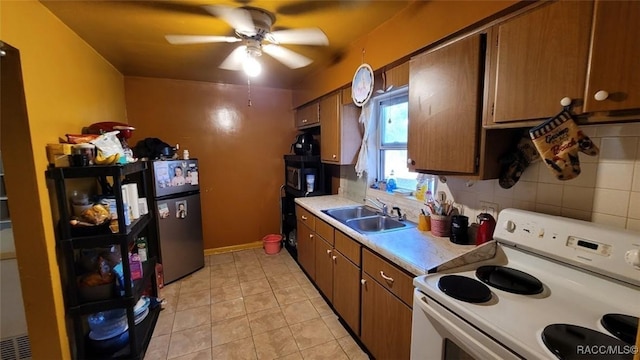 kitchen featuring backsplash, sink, white electric stove, stainless steel fridge, and light tile patterned floors