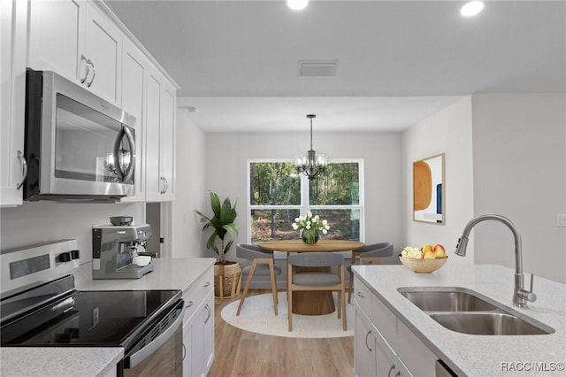 6658 N Bedstrow Blvd, Dunnellon, FL 34434 - kitchen featuring stainless steel appliances, light wood finished floors, white cabinetry, a chandelier, and hanging light fixtures