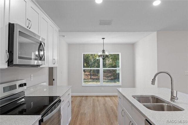 6658 N Bedstrow Blvd, Dunnellon, FL 34434 - kitchen featuring appliances with stainless steel finishes, light wood-style flooring, white cabinetry, a chandelier, and hanging light fixtures