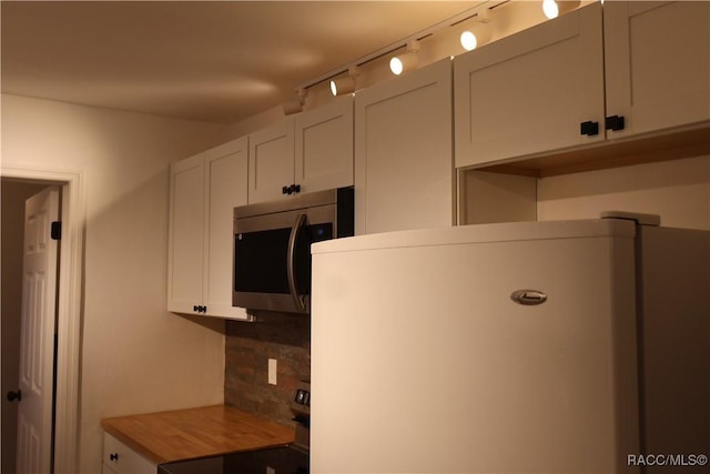 kitchen with white cabinets, refrigerator, and butcher block counters